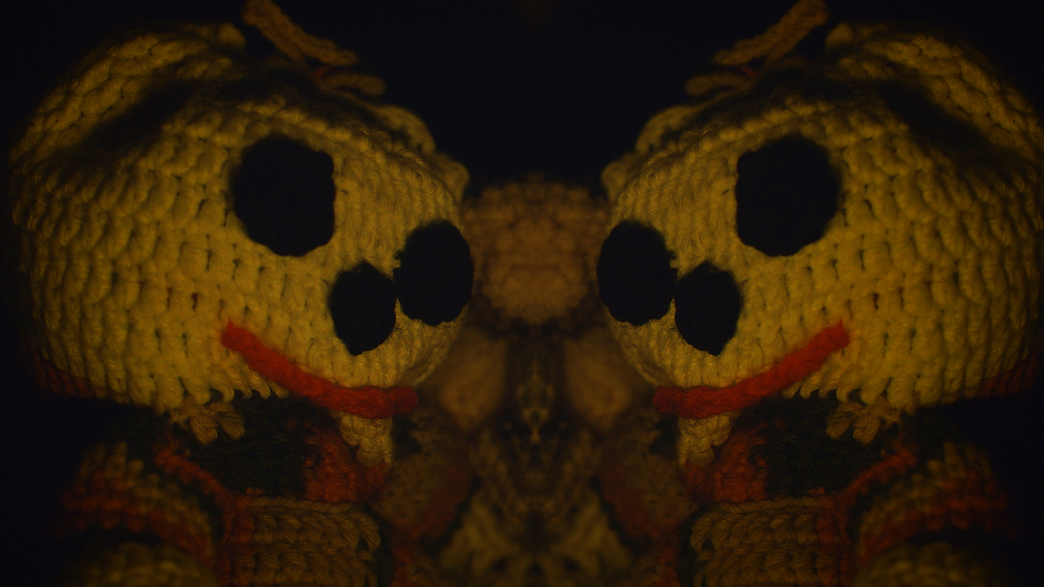 Still from *Night Window* by PJ Raval, 2020

[image description: A mirror image of nasty button faced crocheted devil dolls face each other from within the Night Window realm.]
